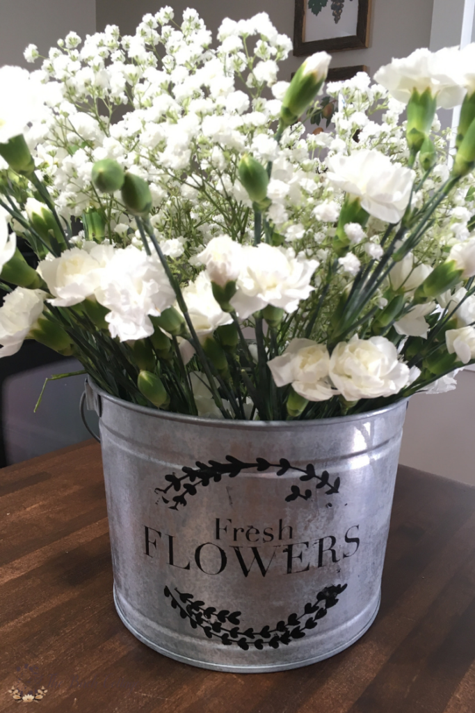 Learn how to stencil a beautiful DIY French flower market galvanized metal bucket using paint, a SVG file and a cutting machine with ideas on how to use it in your home decor. #farmhouse #farmhousedecor #TheSummeryUmbrella #LZCathcart