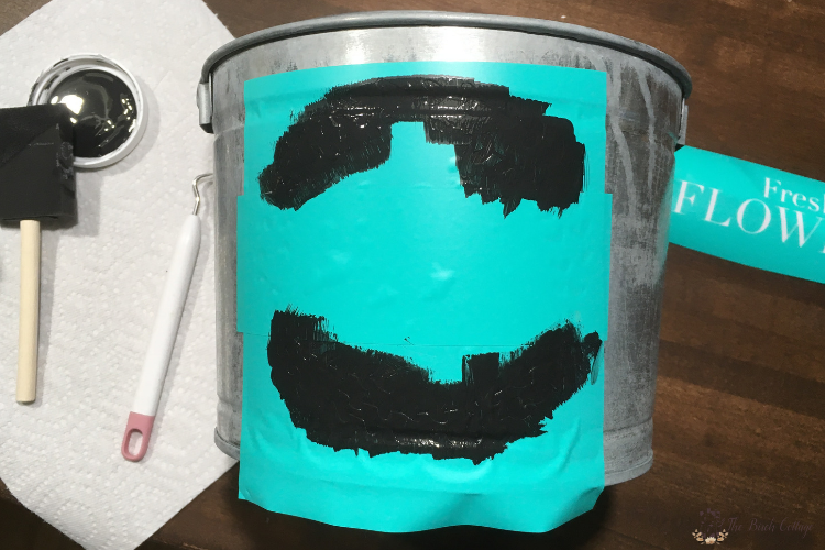 painting a flower market stencil onto a galvanized bucket