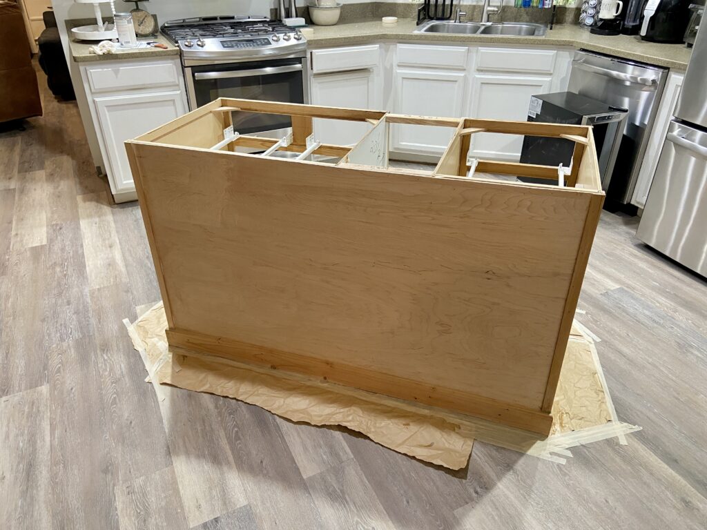 A kitchen island with doors removed, revealing the bare frame ready for painting.