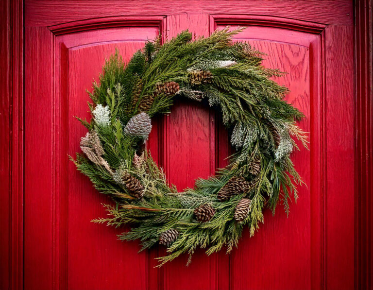 A completed rustic DIY outdoor winter wreath hanging on a red wooden door, featuring burlap ribbon and wooden ornaments.