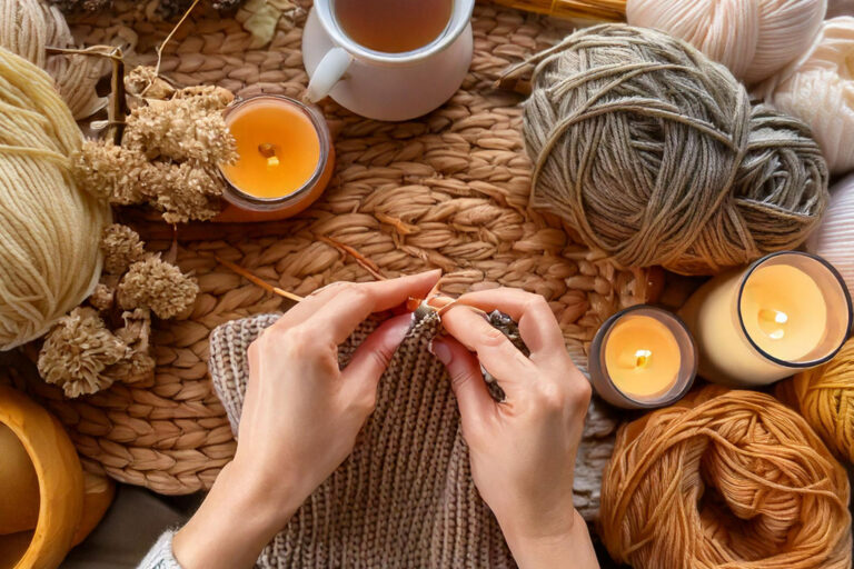 Hands knitting with chunky yarn in a cozy hygge setting