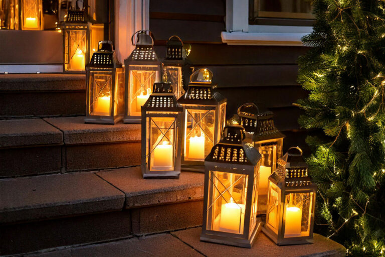 A collection of lanterns in various sizes filled with LED candles, arranged on porch steps with evergreen garlands.